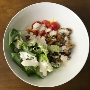 A photo of a white bowl filled with yellow rice, cooked chicken, tomatoes and lettuce